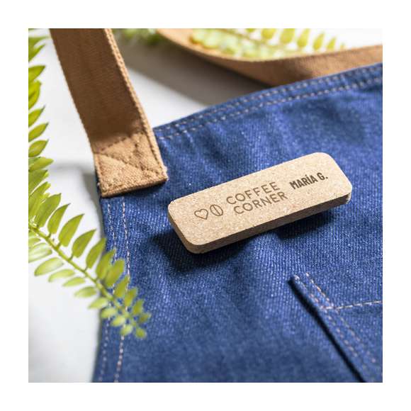 Identificador de línea nature fabricado en corcho natural, para así fomentar la utilización de materias primas naturales y reducir las emisiones contaminantes. Fijación de seguridad con imperdible en la parte trasera.