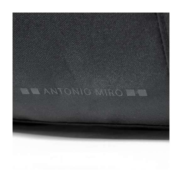 Bolso de Antonio Miró, fabricado en resistente poliéster 300D con acabados en negro. Compartimento principal y bolsillos exteriores con cierre de cremallera a juego  asas de transporte con velcro y bolsillos laterales. Con logotipo de la marca en la base y cinta bandolera ajustable.