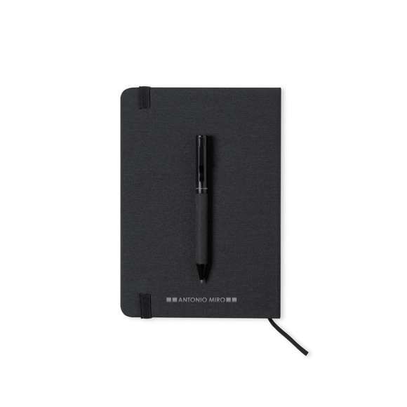 Set de bloc de notas y bolígrafo de Antonio Miró. Incluye:  Bloc de notas de elegante acabado en negro, fabricado en resistente poliéster 300D, con tapas rígidas y elástico de sujeción a juego. Interior con 100 hojas de disposición a una raya.  Bolígrafo metálico de mecanismo giratorio y en tinta azul. Con cuerpo y detalles en negro, clip metálico y logotipo de la marca.  Set presentado en elegante y resistente caja individual negra con logotipo Antonio Miró y funda de protección a juego.