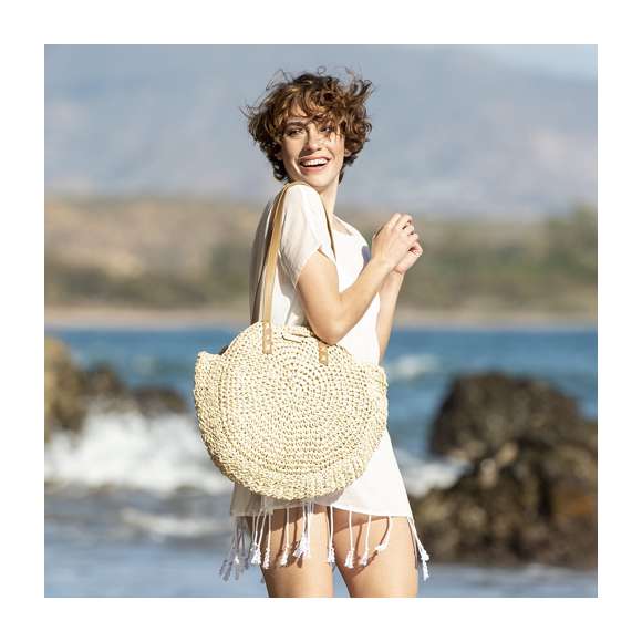 Bolso de desenfadado diseño en rafia sintética y con forma circular, un must. Compartimento principal de cierre de cremallera y tirador metálico, con bolsillo en el interior. Forro interior y asas largas en PU, con triple refuerzo en X y superficie para personalización en madera, especialmente diseñada para marcaje en láser.
