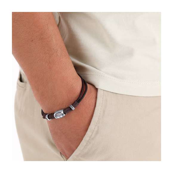 Pulsera de piel marrón adornada con cordones de algodón encerados a juego y abalorios plateados, incluyendo un charm con el símbolo de la paz. Cuenta con un original cierre de aleación de zinc en tono plateado. Presentada en cartón kraft con superficie lisa para el marcaje.