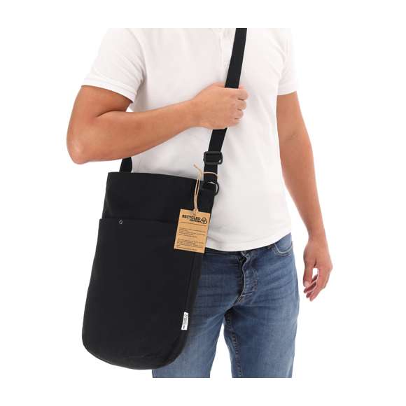 Bolsa fabricada en canvas reciclado de 270g/m2. Original forma cilíndrica de gran capacidad, con compartimento principal, bolsillo auxiliar interior y práctico bolsillo exterior con cierre de broche metálico. En elegante color negro, de acabado cosido y con asa larga reforzada ajustable. Logotipo Algodón Reciclado en etiqueta exterior.