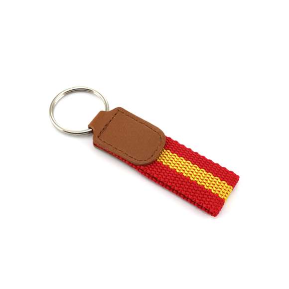 Llavero de poliéster con accesorios de bandera española en la cinta y refuerzo en polipiel de color marrón.