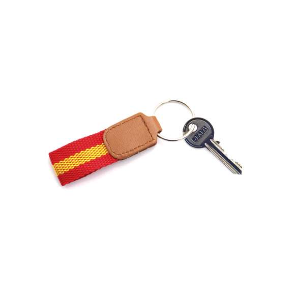 Llavero de poliéster con accesorios de bandera española en la cinta y refuerzo en polipiel de color marrón.