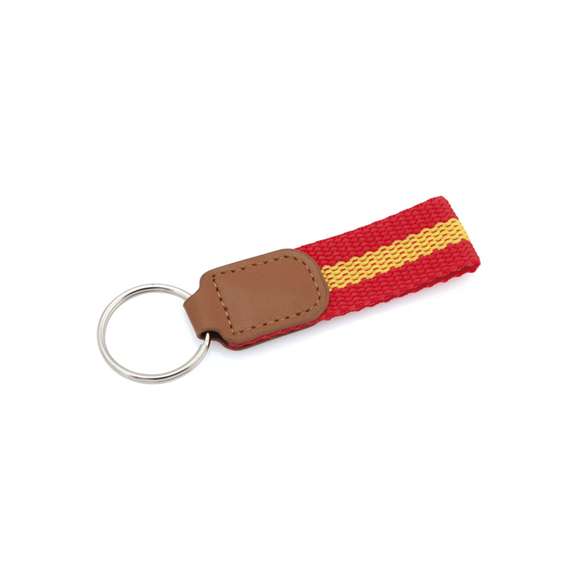 Llavero de poliéster con accesorios de bandera española en la cinta y refuerzo en polipiel de color marrón.