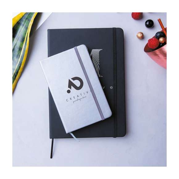 Bloc de notas A5 con tapas duras fabricado en suave polipiel y con 100 hojas lisas. Incluye marcapáginas de tela y banda elástica a juego. Disponible en una extensa gama de colores y presentado en bolsa individual de papel reciclado.
