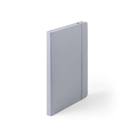 Bloc de notas A5 con tapas duras fabricado en suave polipiel y con 100 hojas lisas. Incluye marcapáginas de tela y banda elástica a juego. Disponible en una extensa gama de colores y presentado en bolsa individual de papel reciclado.