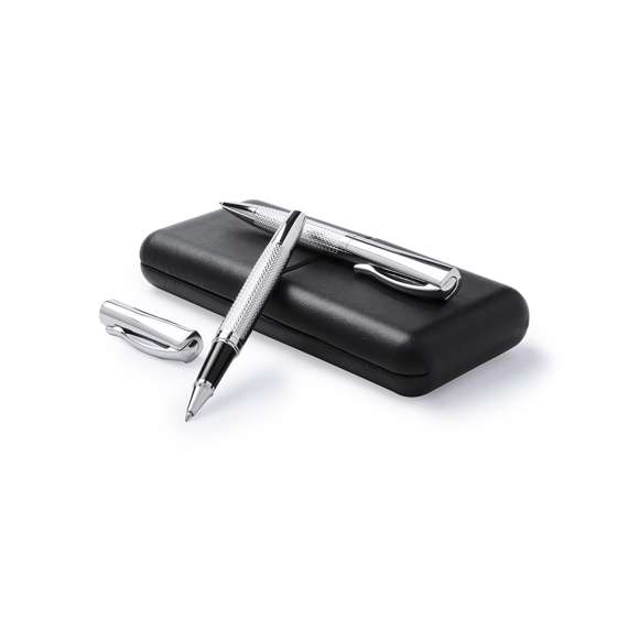 Elegante set de bolígrafo de mecanismo giratorio y roller de capucha en sobrio diseño. De cuerpo metálico antideslizante en acabado plateado brillante con clip a juego. Presentado en elegante y original estuche individual de polipiel en color negro con interior troquelado en suave antelina blanca. De cartucho jumbo con tinta azul de calidad alemana.