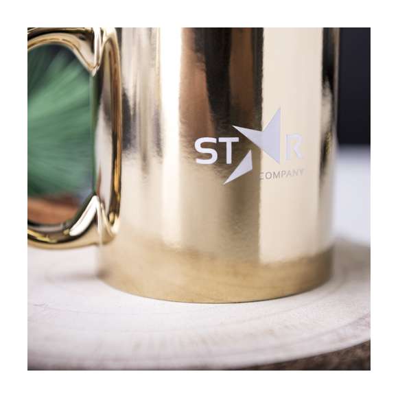Taza de cerámica de 350ml de capacidad. Disponible en llamativos colores plateado y dorado brillantes. Especialmente diseñada para marcaje en láser, con un recubrimiento exterior metalizado especial para que tu publicidad quede perfectamente grabada en color blanco, a juego con el color interior de la taza. Presentada en caja individual. Se desaconseja su uso en el microondas debido al recubrimiento exterior metalizado.