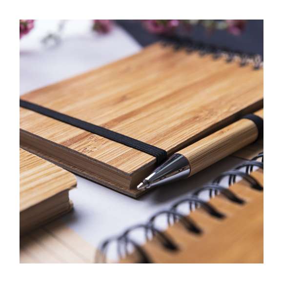  	Libreta de anillas en línea nature con tapas rígidas de bambú y bolígrafo a juego, también en bambú. De tamaño compacto, con elástico de cierre en elegante color negro. Incluye 70 hojas con disposición a una raya y diseño eco. Bolígrafo con cartucho jumbo y tinta azul.