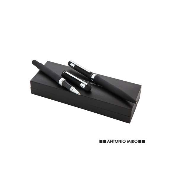 Elegante set de Antonio Miró con bolígrafo de mecanismo giratorio y roller de capucha y original anilla en sobrio diseño. De cuerpo metálico en acabado negro brillante con clip plateado. Presentado en elegante estuche individual en color negro con logotipo de la marca y funda. En tinta azul.
