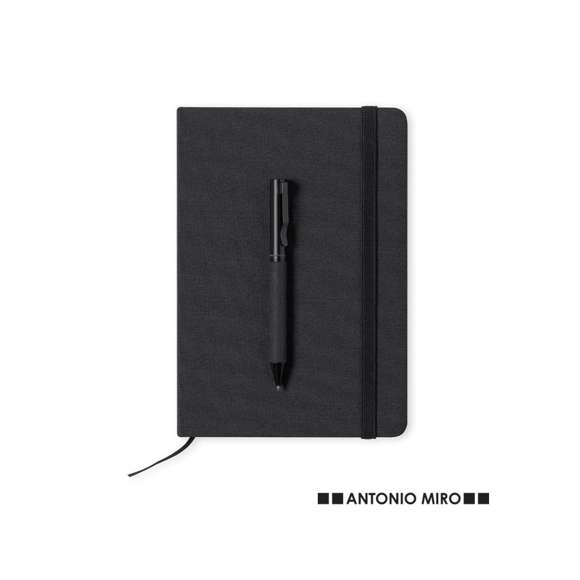 Set de bloc de notas y bolígrafo de Antonio Miró. Incluye:  Bloc de notas de elegante acabado en negro, fabricado en resistente poliéster 300D, con tapas rígidas y elástico de sujeción a juego. Interior con 100 hojas de disposición a una raya.  Bolígrafo metálico de mecanismo giratorio y en tinta azul. Con cuerpo y detalles en negro, clip metálico y logotipo de la marca.  Set presentado en elegante y resistente caja individual negra con logotipo Antonio Miró y funda de protección a juego.